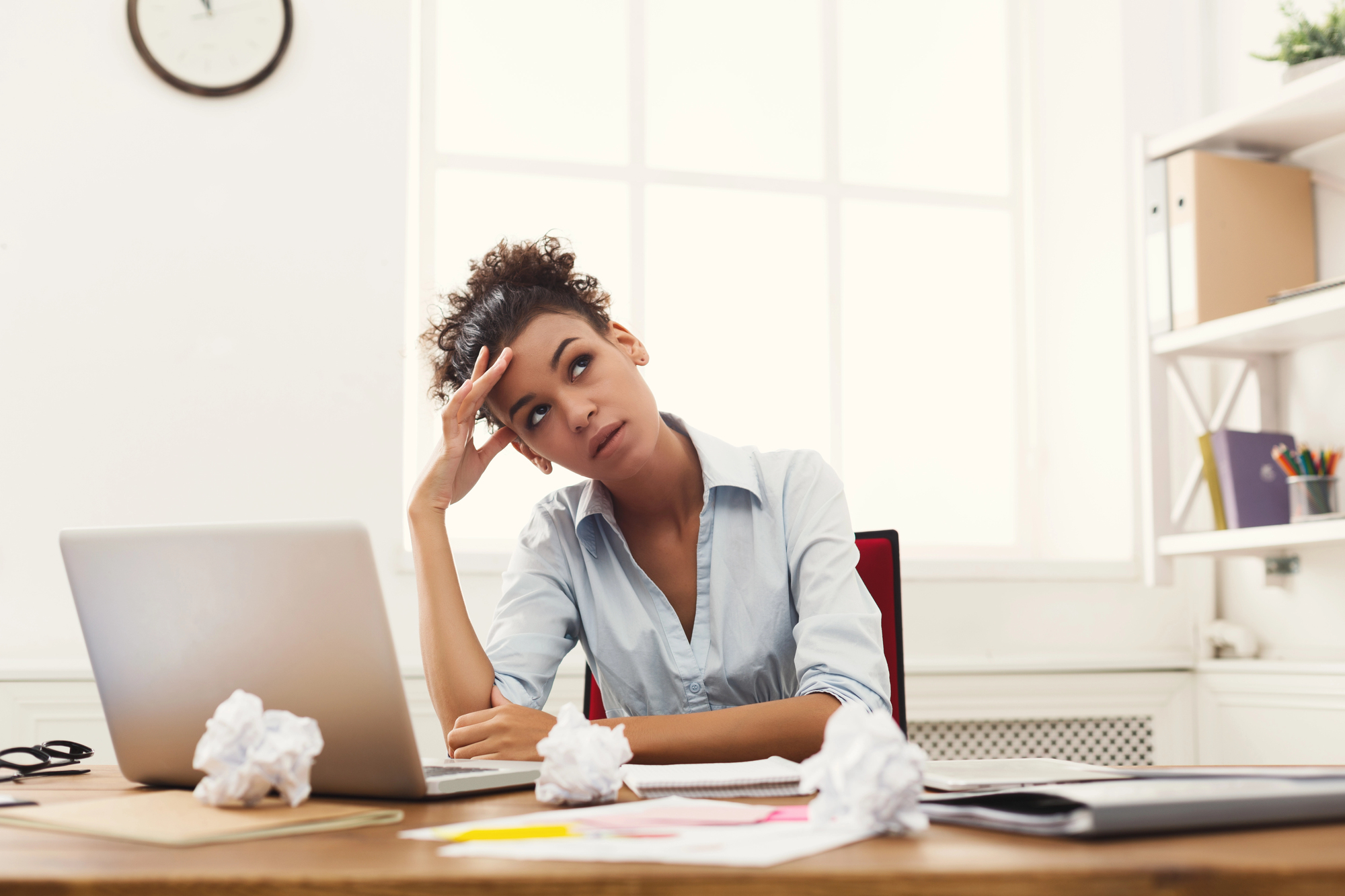Frustrated entrepreneur at her laptop surrounded by crumpled papers